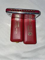 Two Hohner Golden Melody harmonicas showing red plastic combs and gold lettering with key designations and branding, captured from different angles highlighting shiny metal covers and overall condition.