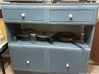 Photo of blue solid wood kitchen hutch cabinet with drawers and open shelf containing pots and pans