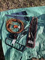 Photo of five saws, orange extension cord, battery charger, and tool pouch laid out on green tarp