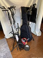Overview of stands, cables, guitar case, coffee can, music stand and lamp