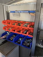 Parts bin filled with assorted metal hardware items in red and blue bins on a metal frame