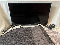 Samsung 31 inch TV with remote control and power cord placed on carpeted surface against white backdrop.