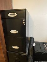 Black metal 3-drawer filing cabinet with silver handles and key in lock
