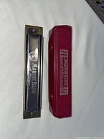 Top view of Hohner Marine Band harmonica next to its red carrying case showing branding on both.