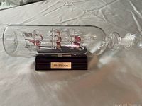 Glass model of HMS Victory in a glass bottle on wooden stand with name plaque
