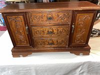 Front view of the wood jewelry chest showing carved floral designs on two doors and three drawers with metal handles.