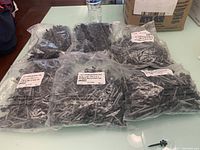 Six clear plastic bags containing black roofing screws, four bags labeled as 2-inch screws, two bags labeled as 1.5-inch screws, each bag containing 250 screws.