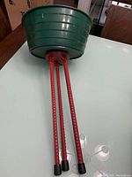 Green plastic Christmas tree base showing the red metal legs folded beneath