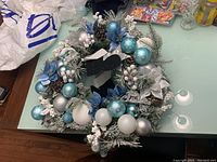 Round Christmas wreath decorated in blue, silver, and white with pinecones and frosted branches.
