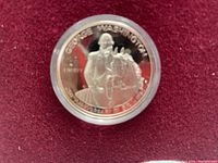 Photo showing front side of George Washington commemorative coin with inscription 'GEORGE WASHINGTON', 'LIBERTY', and the image of him on horseback, set against a red background.
