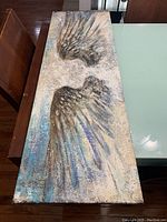 Front view of angel wings wall art showing textured painting with brown, blue, and beige tones