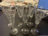 View of six Waterford crystal champagne flutes showing detailed cut designs on the bowls and clear long stems.