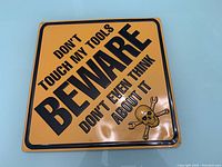 Front view of 13x13 inch yellow metal sign with black warning text and skull with crossed wrenches graphic.