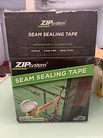 Closed box showing the product name and branding: ZIP System Seam Sealing Tape with advanced acrylic flashing tape, containing 12 rolls each measuring 3-3/4 inches by 90 feet.