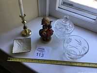 Overview of all items on bureau top including brass candlestick holder, Goebel figurine, cut glass containers, and Lenox jewelry holder