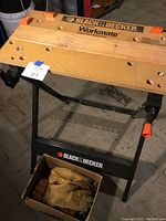 Black and Decker branded Workmate portable project center and vise, wooden top surface with holes for clamping, black metal frame.