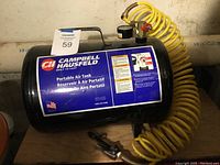 Full side view of a black Campbell Hausfeld portable air tank with label and attached yellow coiled air hose.