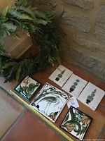 Set of six decorative hand-painted ceramic wall tiles arranged on floor with measuring tape for scale, three topiary-themed and three Salamon floral designs.