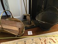 Photo showing the coal bucket, brass colored wood holder with firewood logs, and part of the fireplace tool stand base.