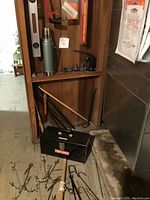 Overview shot showing Craftsman toolbox, green thermos, yellow spirit level on wall, and various long wooden and metal tools behind.