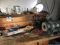 Overview of work bench showing saw, bench grinder, hammers, wire brush and screwdriver bits