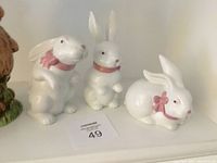 Photo showing three white ceramic rabbit figurines with pink bows, depicting sitting, standing, and crouching poses.