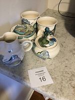 View of all five pottery items arranged on counter including mugs, creamer, sugar bowl, and butter dish with hand-painted designs.