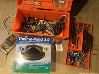 Orange plastic Tuff Box open showing various boat tools and hardware, including metal chains, pulleys, and clips loosely stored inside compartments.