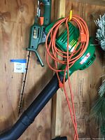 Overview photo of the green Black and Decker Autostop trimmer, leaf blower, and orange extension cord.
