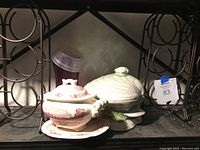 Two metal wine racks, ceramic soup tureen with lid and underplate, and clam shell lidded ceramic decoration on metal shelf