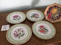 Four Winterthur adaption plates with scalloped rims, mint green borders, gold-colored ornate trim, and central botanical floral imagery.