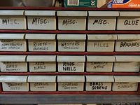 Front view of 29 slot organizer with labeled drawers containing various nails, screws, brushes, files, and glue.