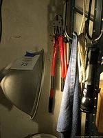 Photo of red-handled limb trimmer and 18-inch wire cutters hanging on a rack along with flashlight and towel.