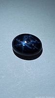 Close-up photo of a polished oval cabochon blue star sapphire with visible star asterism effect on its deep blue surface.