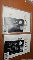 Top view of two moissanite earrings with GRA certification cards showing warranty ID, stone size 7.0mm, and carat weight 1.2ct each.