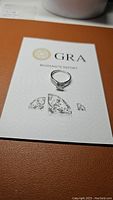 Ring placed on a GRA Moissanite Report certificate showing the certification details.