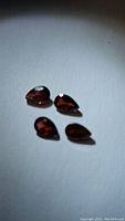 Four pear-shaped deep red garnet gemstones on a white surface, showing faceting and overall shape.
