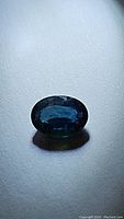 Oval cut blue sapphire photographed on a flat surface showing its deep blue color and faceted cut.