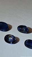 Four oval cut dark blue sapphires on a white textured surface, one showing a full rainbow inclusion