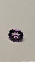Close-up of a 3.51ct natural Brazilian amethyst oval cut gemstone on a white background showing its color and facets.