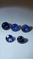 Five round faceted natural blue sapphire stones, royal blue color, various angles under light revealing clarity and cut.