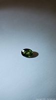 Oval cut natural chameleon green sapphire gemstone showing rich green color and faceting details on plain background.