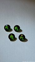 Four round green chrome diopside gemstones displayed on a flat surface under light, showing deep vibrant green color.