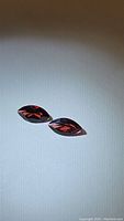 Two marquis cut garnet gemstones displayed on a white surface with visible facets showing red-orange color.