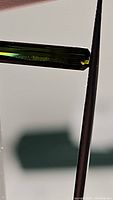 Close-up photo of the slim elongated octagon cut green tourmaline held with tweezers showing green color and clarity.