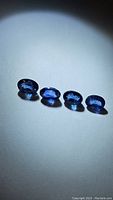 Four oval-cut natural royal blue sapphires arranged in a line on a plain white surface under light, showing their color and clarity.