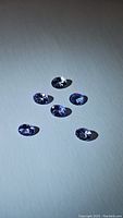 Five oval cut blue-purple tanzanite gemstones arranged on a light surface showing clarity and color.