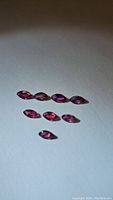 Eight natural untreated rubies in marquis cut, pink to purple hues on white background.
