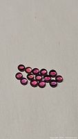 Thirteen round cabochon sapphires displayed on white background showing vibrant red to hot pink colors with high clarity.