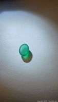 Oval vivid green onyx cabochon gemstone under spot light showing color and translucency on white background.